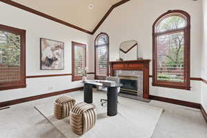 Carpeted home office featuring vaulted ceiling, a fireplace, and ornamental molding