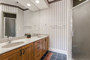 Bathroom featuring double vanity, a shower stall, wallpapered walls, dark tile patterned flooring, and ornamental molding