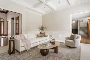 Carpeted living room with crown molding, coffered ceiling, a wainscoted wall, and a decorative wall