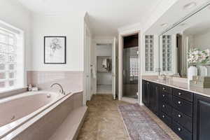 Bathroom featuring double vanity, a spacious closet, ornamental molding, a garden tub, and a stall shower
