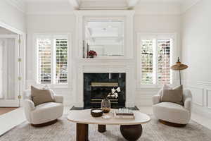 Sitting room featuring a decorative wall, wainscoting, a premium fireplace, crown molding, and healthy amount of natural light