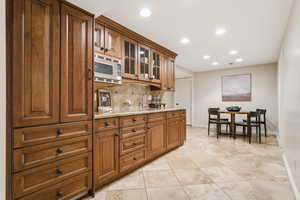 Kitchen with light stone countertops, wood finish cabinets, recessed lighting, glass insert cabinets, and built in microwave
