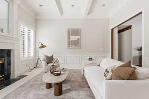 Living area featuring a premium fireplace, wainscoting, ornamental molding, a decorative wall, and beam ceiling