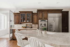 Kitchen featuring high end fridge, dark wood finish cabinetry, glass fronted cabinets, light wood-style floors, and tasteful backsplash