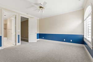 Empty room with ornamental molding, a ceiling fan, and light carpet