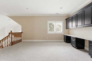 Unfurnished office featuring ornamental molding, built in study area, and light colored carpet