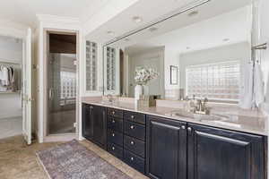 Bathroom with crown molding, double vanity, a shower stall, and a walk in closet