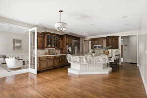 Kitchen with dark wood finish cabinets, a kitchen bar, a center island with sink, and dark wood-style floors