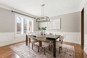 Dining room with hardwood / wood-style flooring, a wainscoted wall, ornamental molding, and a decorative wall