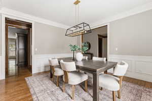Dining area featuring ornamental molding, hanging lights, wood finished floors, and a wainscoted wall