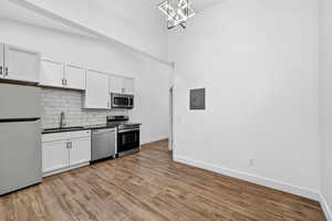 Kitchen featuring dark countertops, stainless steel appliances, white cabinetry, decorative backsplash, and light wood-type flooring