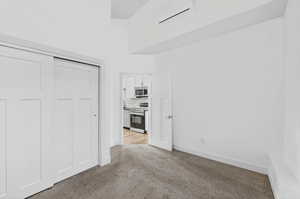 Unfurnished bedroom with a closet, light colored carpet, and a high ceiling