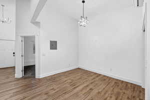Unfurnished dining area featuring suspended lighting, a high ceiling, dark wood-type flooring, and electric panel