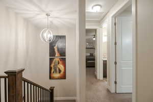 Corridor featuring light colored carpet and hanging lights