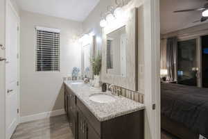 Ensuite bathroom featuring double vanity, light wood finished floors, and a ceiling fan