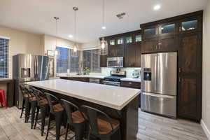 Kitchen with stainless steel appliances, a kitchen bar, dark wood finish cabinets, hanging light fixtures, and a center island