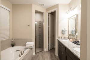 Bathroom featuring double vanity, a garden tub, a shower stall, and light wood-style flooring