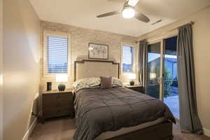 Bedroom with a ceiling fan, access to exterior, dark carpet, and brick wall