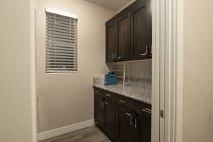 Bar featuring dark wood finish cabinets, light stone countertops, and light wood-style flooring