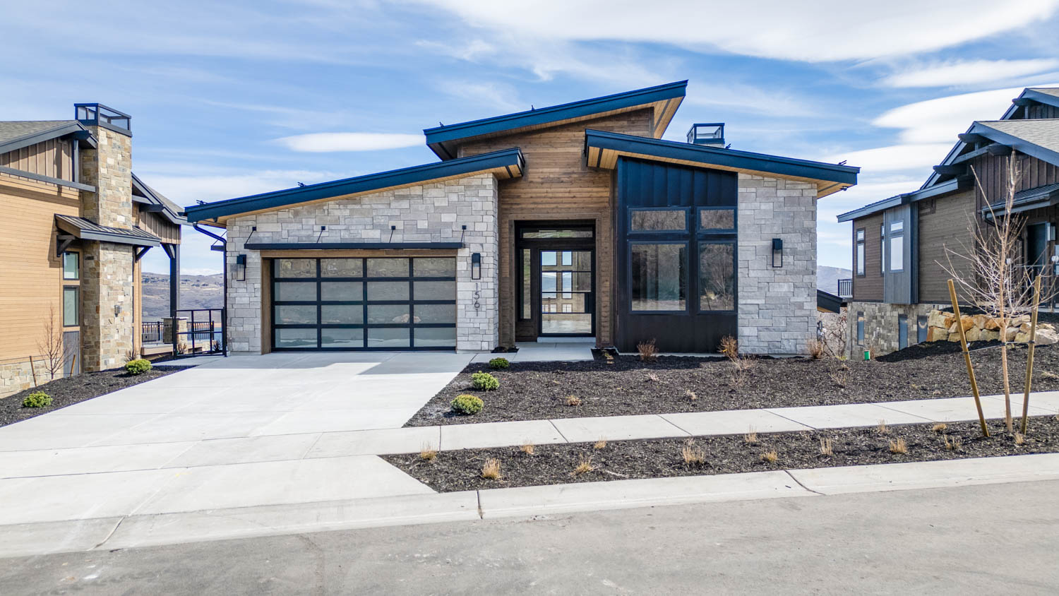 Contemporary house with stone siding, a garage, and concrete driveway