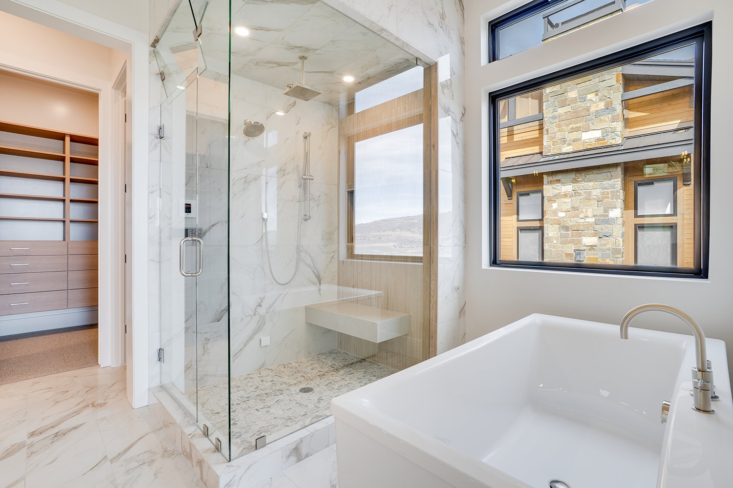 Full bathroom featuring a marble finish shower, a freestanding tub, a spacious closet, and light marble finish flooring