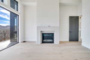 Unfurnished Primary Bedroom featuring light wood-style flooring, a high ceiling, and a glass covered fireplace