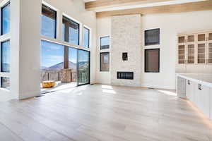 Unfurnished living room with a mountain view, a stone fireplace, light wood-type flooring, and lofted ceiling
