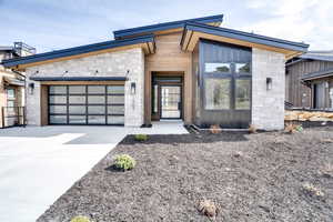 Modern home featuring an attached garage, stone siding, concrete driveway, and board and batten siding