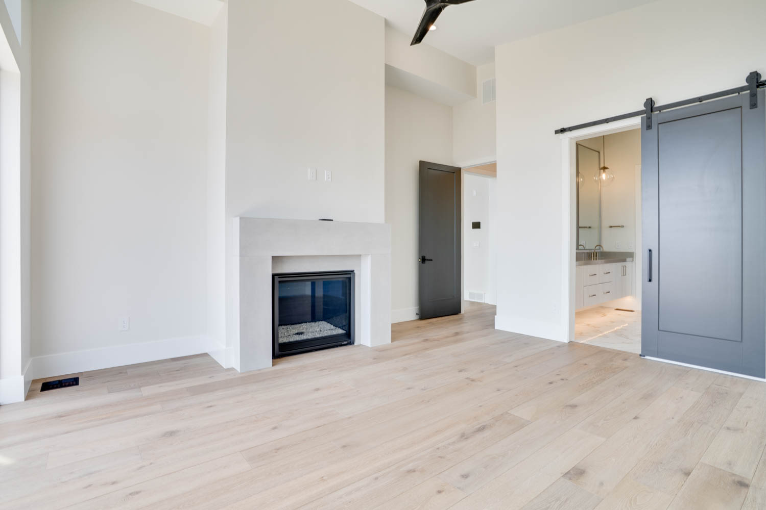 Unfurnished Primary Bedroom featuring a barn door, a high ceiling, light wood finished floors, and a glass covered fireplace