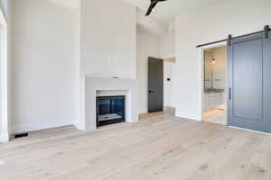 Unfurnished Primary Bedroom featuring a barn door, a high ceiling, light wood finished floors, and a glass covered fireplace