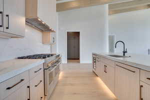 Kitchen featuring light stone countertops, range with two ovens, light wood finish cabinetry, and beam ceiling
