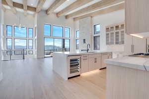 Kitchen with light stone countertops, wine cooler, a mountain view, light wood-style floors, and glass insert cabinets