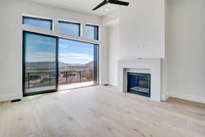 Unfurnished Primary Brdroom with a high ceiling, a mountain view, a glass covered fireplace, ceiling fan, and light wood-type flooring