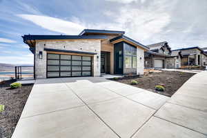 Contemporary home with stone siding, a garage, concrete driveway, and board and batten siding
