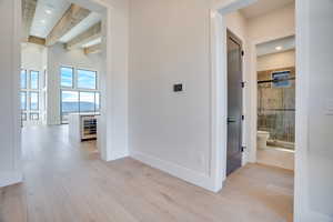 Hallway with recessed lighting, light wood-style floors, beamed ceiling, and beverage cooler