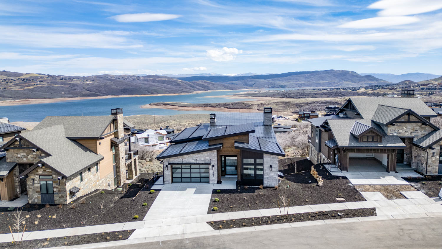 View of front of house with stone siding, a chimney, a water and mountain view, roof mounted solar panels, and concrete driveway