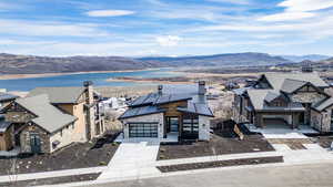 View of front of house with stone siding, a chimney, a water and mountain view, roof mounted solar panels, and concrete driveway