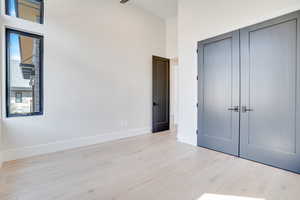 Unfurnished bedroom featuring light wood-style floors, a high ceiling, and a closet