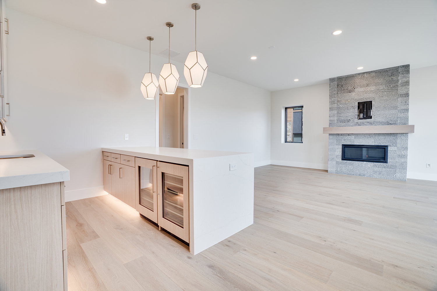 Kitchen with light stone countertops, light wood-style floors, beverage cooler, light wood finish cabinets, and modern cabinets