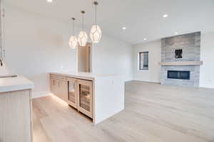 Kitchen with light stone countertops, light wood-style floors, beverage cooler, light wood finish cabinets, and modern cabinets