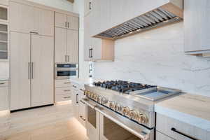 Kitchen with stainless steel appliances, light wood finish cabinetry, light wood-style flooring, light stone countertops, and decorative backsplash