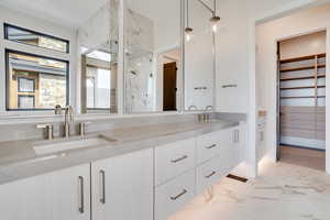 Full bathroom featuring double vanity, a marble finish shower, a spacious closet, and light marble finish floors