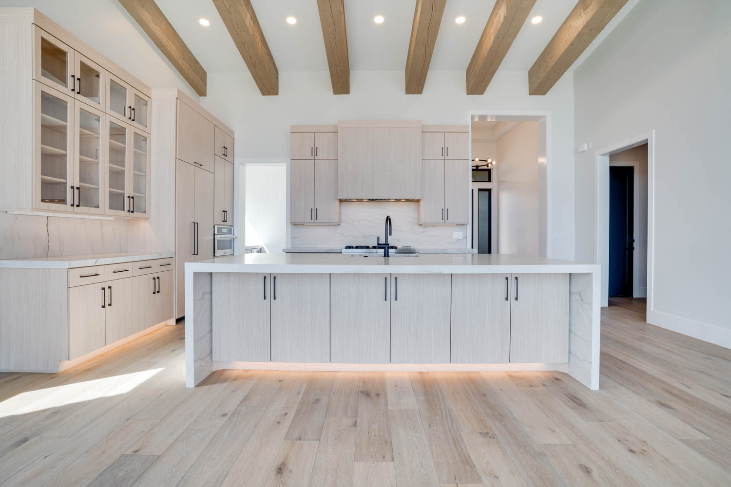 Kitchen with recessed lighting, glass insert cabinets, a large island with sink, light wood-style floors, and light wood finish cabinets