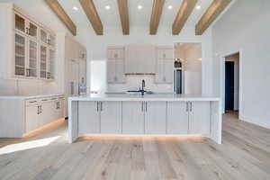 Kitchen with recessed lighting, glass insert cabinets, a large island with sink, light wood-style floors, and light wood finish cabinets