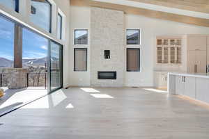Unfurnished living room with a mountain view, light wood finished floors, lofted ceiling, and a stone fireplace