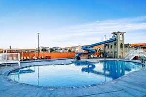 Community pool with a water slide, a residential view, and a patio
