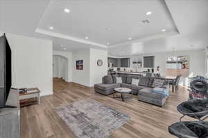 Living room featuring a tray ceiling, light wood-style floors, arched walkways, and a chandelier