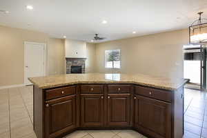 Kitchen with a kitchen island, light tile patterned floors, a stone fireplace, ceiling fan, and open floor plan