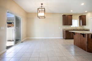Kitchen featuring a breakfast bar, light stone countertops, light tile patterned floors, dark wood finish cabinets, and a chandelier