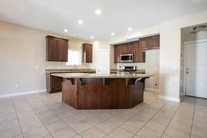 Kitchen with a kitchen bar, light stone countertops, light tile patterned flooring, a center island, and recessed lighting